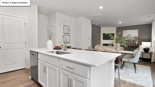 kitchen featuring light wood-type flooring, dishwasher, a kitchen island with sink, sink, and white cabinetry