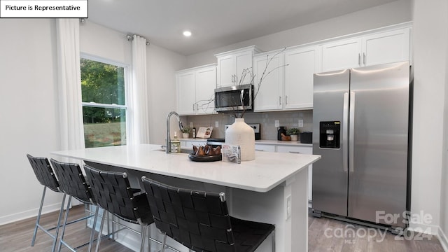 kitchen with light hardwood / wood-style floors, a kitchen island with sink, white cabinets, a kitchen breakfast bar, and stainless steel appliances