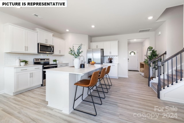 kitchen with backsplash, a kitchen island with sink, white cabinets, light hardwood / wood-style flooring, and stainless steel appliances