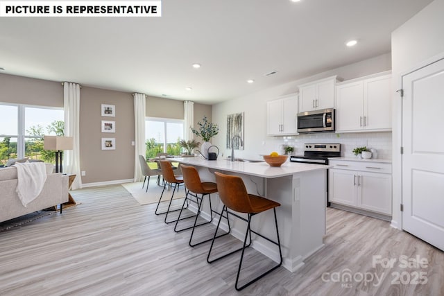 kitchen with a sink, a kitchen breakfast bar, appliances with stainless steel finishes, tasteful backsplash, and an island with sink