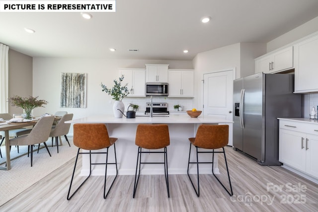 kitchen with white cabinets, appliances with stainless steel finishes, a breakfast bar, and light countertops