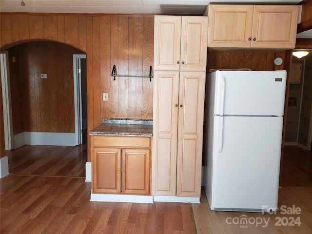 kitchen featuring wood-type flooring, white refrigerator, and wooden walls