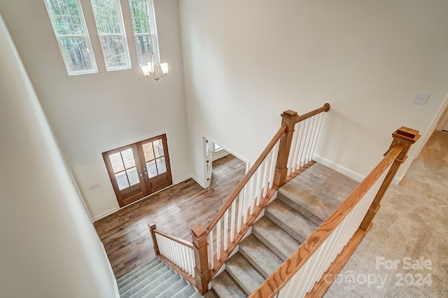 staircase featuring french doors, a chandelier, hardwood / wood-style floors, and a high ceiling