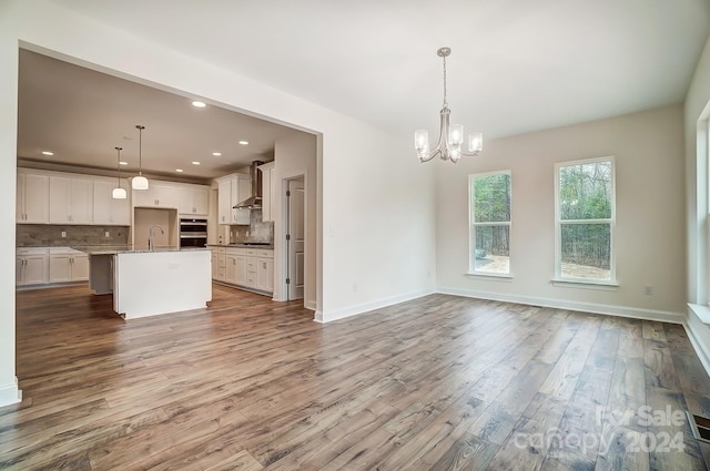 kitchen featuring light hardwood / wood-style flooring, wall chimney range hood, an island with sink, and decorative light fixtures