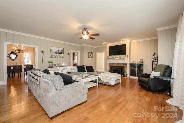 living room with light hardwood / wood-style flooring, ceiling fan with notable chandelier, a fireplace, and crown molding