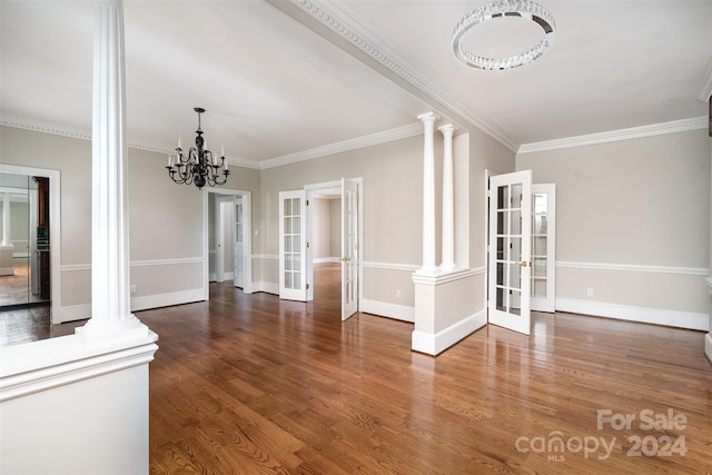 unfurnished dining area featuring ornamental molding, french doors, a chandelier, dark wood-type flooring, and ornate columns