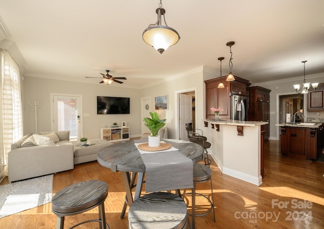 dining room with ceiling fan with notable chandelier, light wood-type flooring, sink, and crown molding