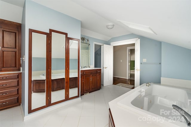 bathroom featuring tile patterned flooring, a tub to relax in, vaulted ceiling, and vanity