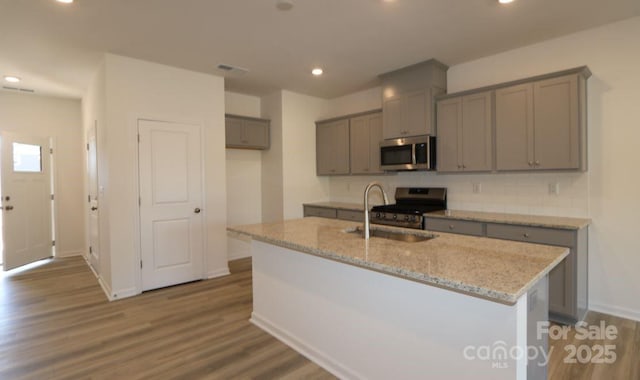 kitchen with sink, gray cabinets, an island with sink, hardwood / wood-style flooring, and stainless steel appliances