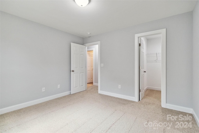 unfurnished bedroom with a spacious closet, light carpet, and a closet