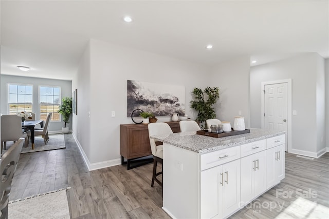 1038 Heath Helms Rd, Monroe, NC 28110 - kitchen with light wood finished floors, a kitchen island, light stone counters, a breakfast bar area, and white cabinetry