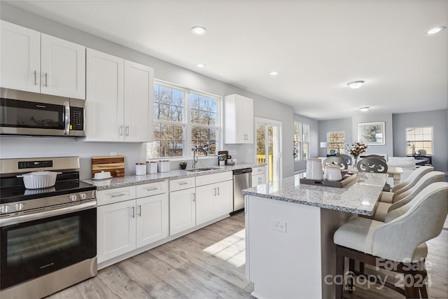 1038 Heath Helms Rd, Monroe, NC 28110 - kitchen with appliances with stainless steel finishes, a kitchen island, a breakfast bar area, light wood-type flooring, and white cabinets