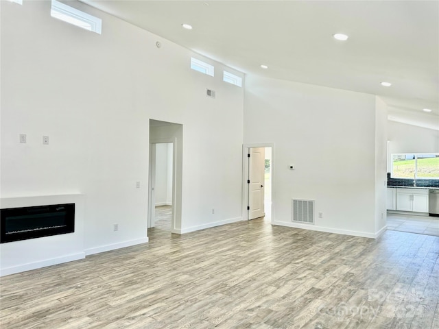 unfurnished living room featuring visible vents, light wood finished floors, and high vaulted ceiling