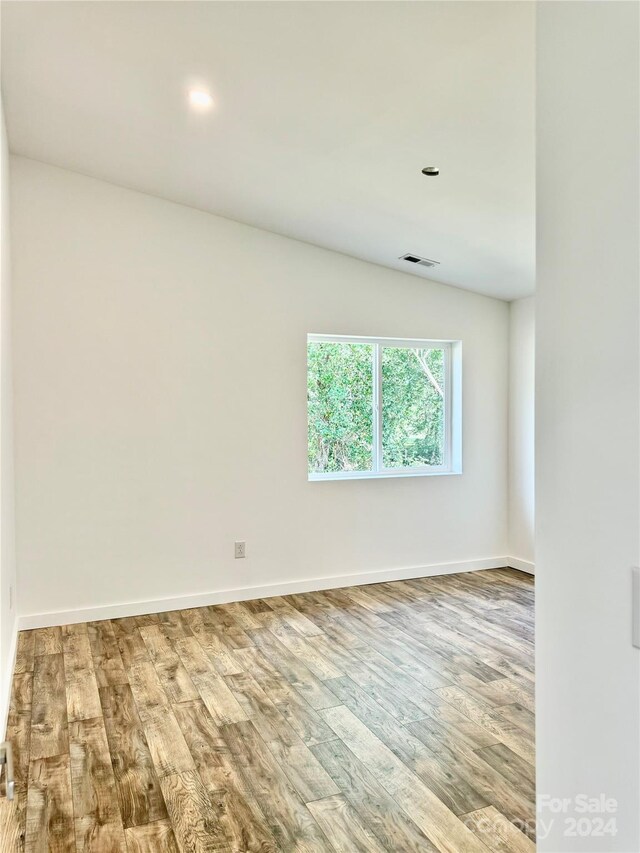 spare room featuring wood-type flooring and lofted ceiling