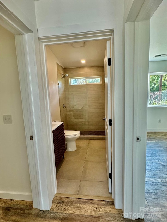 bathroom with a tile shower, vanity, toilet, and hardwood / wood-style flooring