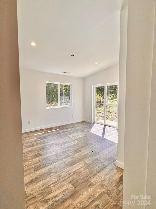 unfurnished room with a healthy amount of sunlight, vaulted ceiling, and wood-type flooring