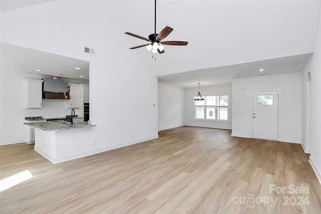 unfurnished living room featuring sink, high vaulted ceiling, light hardwood / wood-style floors, and ceiling fan with notable chandelier