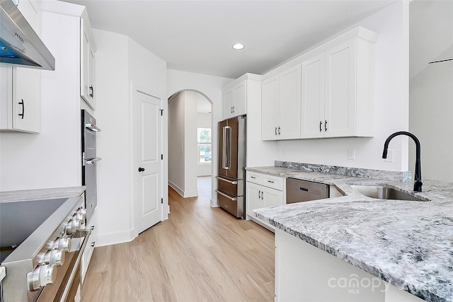 kitchen featuring arched walkways, light stone counters, stainless steel appliances, wall chimney range hood, and a sink