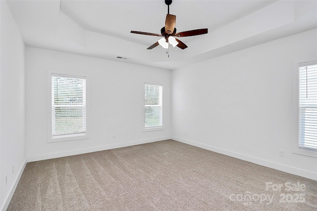 empty room featuring carpet, visible vents, a tray ceiling, and baseboards