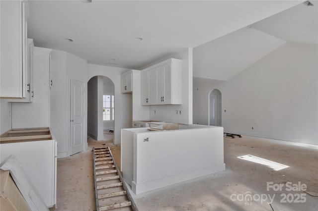 kitchen featuring arched walkways, vaulted ceiling, and white cabinets