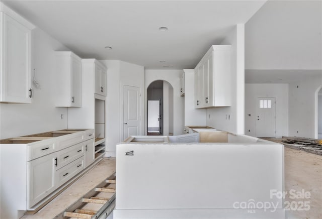 kitchen featuring a kitchen island, arched walkways, and white cabinets