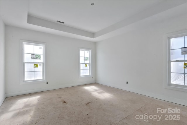 spare room with a tray ceiling, visible vents, and baseboards