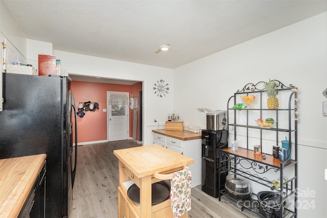 kitchen with white cabinetry, wood counters, light hardwood / wood-style flooring, and black refrigerator