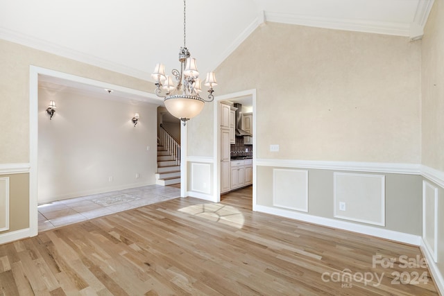 spare room with ornamental molding, an inviting chandelier, light hardwood / wood-style floors, and high vaulted ceiling