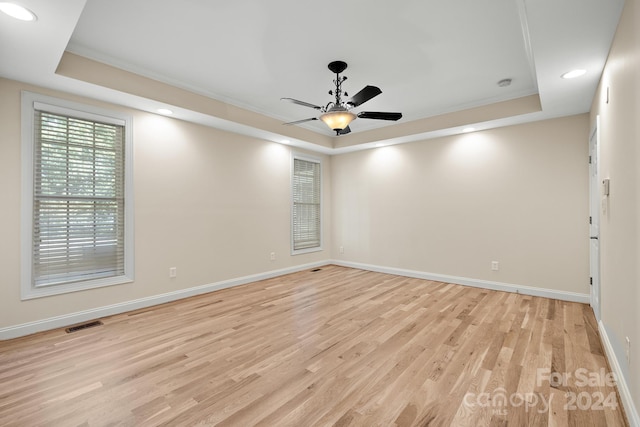 unfurnished room with ceiling fan, a tray ceiling, ornamental molding, and light hardwood / wood-style flooring