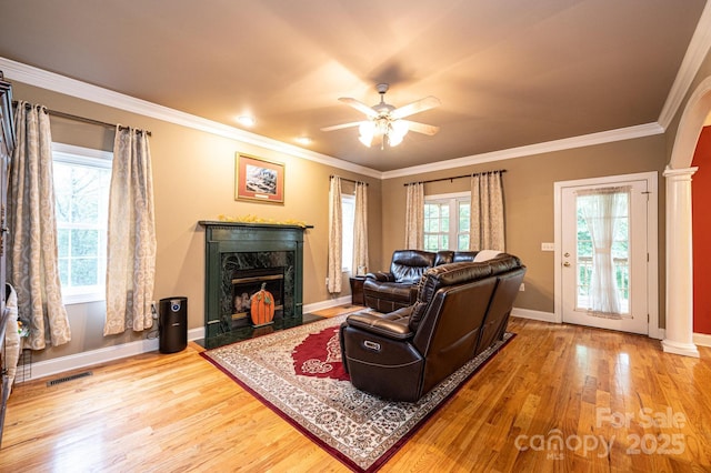 living room featuring ceiling fan, ornamental molding, a high end fireplace, and decorative columns