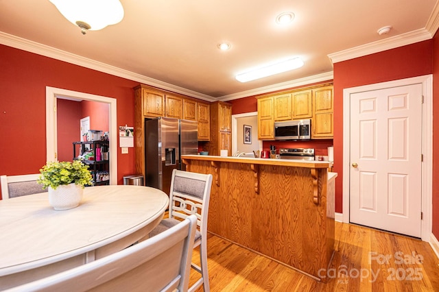 kitchen with kitchen peninsula, appliances with stainless steel finishes, light hardwood / wood-style flooring, and crown molding