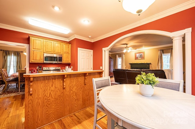 kitchen with decorative columns, stainless steel appliances, ceiling fan, crown molding, and light hardwood / wood-style flooring