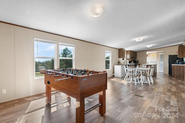 rec room featuring a textured ceiling, light hardwood / wood-style flooring, and vaulted ceiling