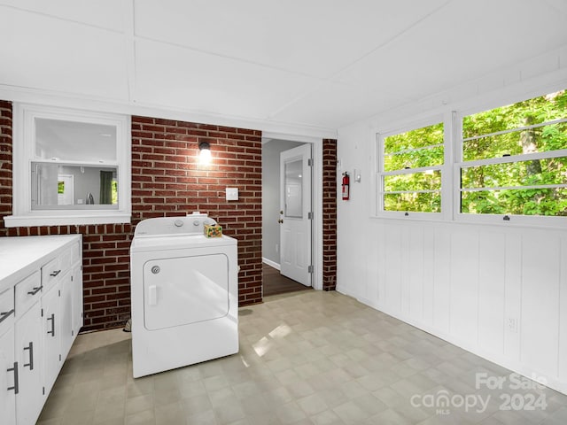 washroom with brick wall, cabinets, and washer / dryer