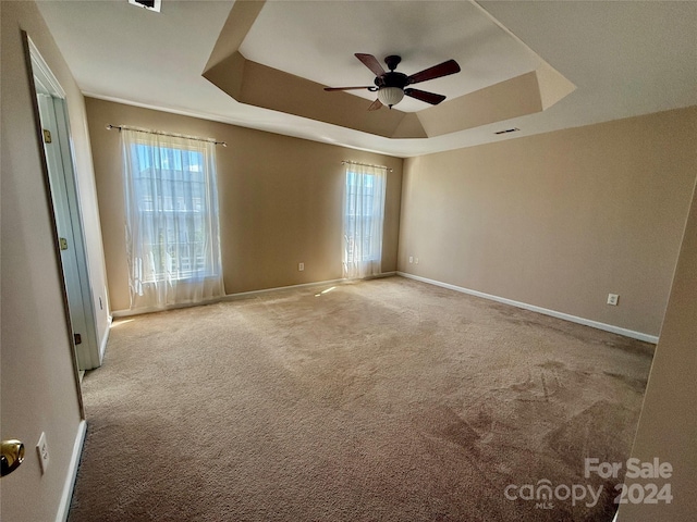 carpeted spare room featuring ceiling fan and a raised ceiling