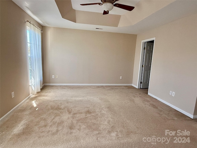 carpeted empty room with ceiling fan and a tray ceiling