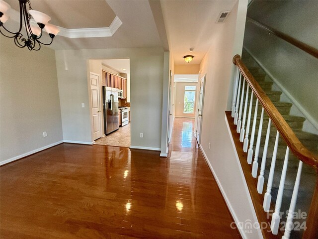 interior space featuring wood-type flooring, ornamental molding, and an inviting chandelier