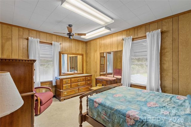 carpeted bedroom featuring multiple windows, ceiling fan, and wood walls