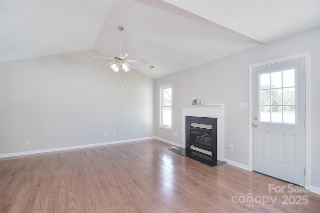 unfurnished living room with ceiling fan, a glass covered fireplace, vaulted ceiling, wood finished floors, and baseboards