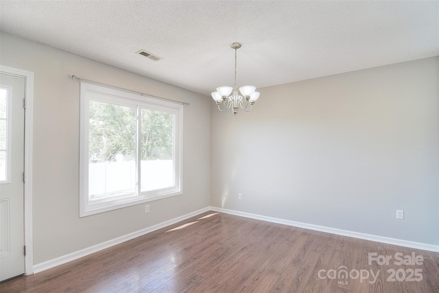 spare room featuring visible vents, baseboards, a notable chandelier, a textured ceiling, and wood finished floors