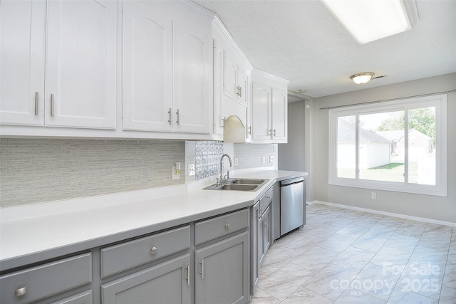 kitchen with light countertops, gray cabinetry, stainless steel dishwasher, marble finish floor, and a sink