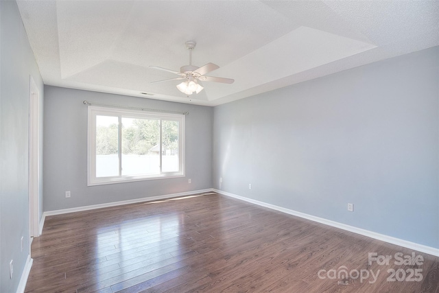 empty room with baseboards, a raised ceiling, visible vents, dark wood finished floors, and ceiling fan