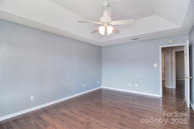 unfurnished room with a ceiling fan, visible vents, wood finished floors, a raised ceiling, and baseboards