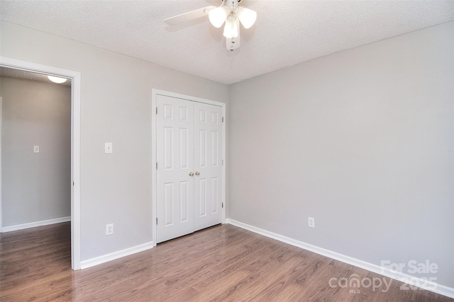 unfurnished bedroom with a textured ceiling, a closet, a ceiling fan, wood finished floors, and baseboards