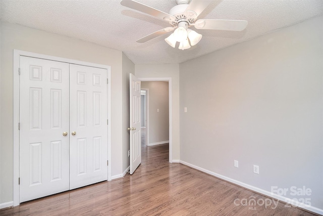 unfurnished bedroom featuring a textured ceiling, wood finished floors, a closet, and baseboards