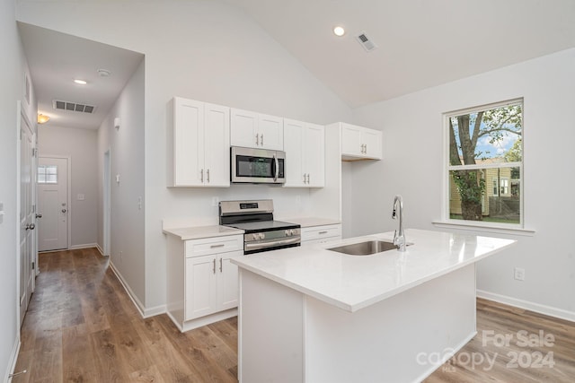 kitchen with an island with sink, sink, white cabinetry, appliances with stainless steel finishes, and vaulted ceiling