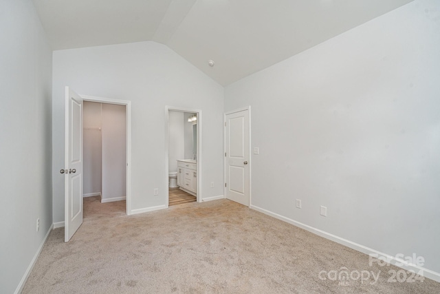 unfurnished bedroom with lofted ceiling, ensuite bathroom, and light colored carpet