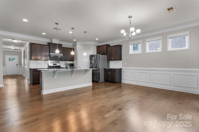 kitchen with appliances with stainless steel finishes, an island with sink, a kitchen breakfast bar, hanging light fixtures, and dark brown cabinets