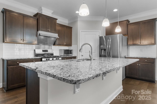 kitchen with appliances with stainless steel finishes, pendant lighting, sink, a kitchen breakfast bar, and a kitchen island with sink