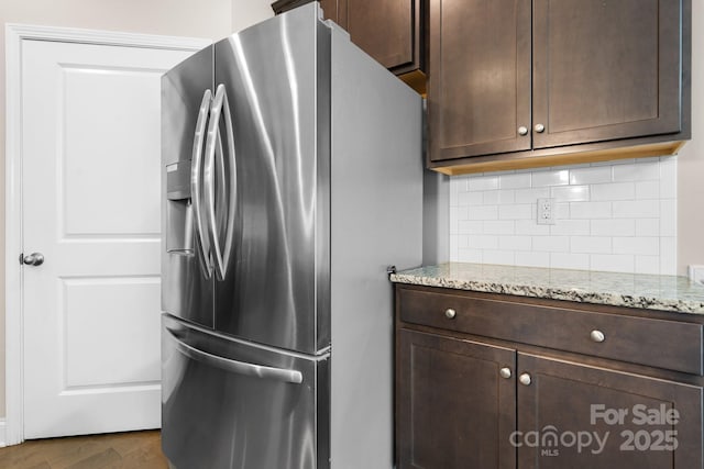 kitchen with dark brown cabinetry, stainless steel fridge, and light stone counters